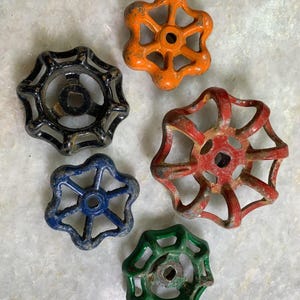 May include: Five vintage metal water valve handles in various colors. The handles are star-shaped with a circular opening in the center. The colors are orange, black, red, blue, and green.