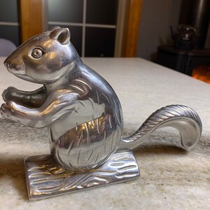 May include: A silver squirrel nutcracker with a detailed design. The squirrel is standing on a base with a woodgrain texture.