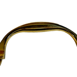 May include: A gold-colored cabinet pull handle with a curved bar and oval mounting plates. Each plate has three screw holes. The handle is made of metal and has a shiny finish.