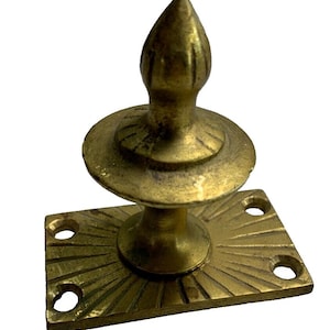 May include: A brass door handle with a decorative, pointed finial and a rectangular base with a sunburst design.