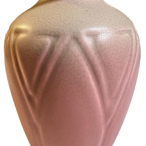 May include: A pink ceramic vase with a textured surface and a flared, rounded shape. The vase has a wide opening and a decorative pattern of vertical lines. The color gradient transitions from a light pink at the top to a deeper pink at the base.