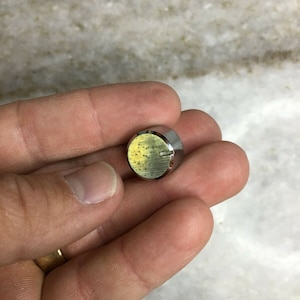 Peut inclure: Un bouton rond de couleur argentée avec une surface texturée et une petite rainure autour du bord.