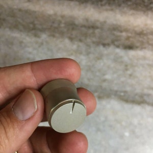 Puede incluir: Un pomo plateado con una pequeña línea blanca en la parte superior. El pomo es redondo y tiene una superficie lisa.