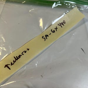 Puede incluir: Una bolsa de plástico transparente con cierre de cremallera verde. En el interior, una tira de papel amarilla muestra el texto manuscrito "SA-6x490" y "Teclares" en tinta negra. El papel está ligeramente inclinado.