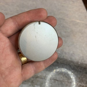 Puede incluir: Un pomo redondo plateado con una pequeña ranura en la parte superior.