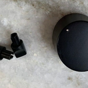 Puede incluir: Una perilla negra con un pequeño botón redondo plateado en el centro. También se muestran tres perillas de plástico negro con un pequeño botón redondo plateado en el centro.