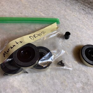 Puede incluir: Una bolsa de plástico transparente que contiene cinco pies de tocadiscos negros y plateados, un pie de plástico negro y un trozo de papel con el texto "Marantz DR4050" escrito en él.