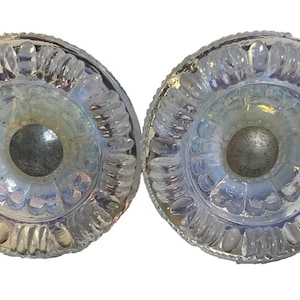 May include: Two circular glass door knobs featuring a clear, iridescent finish with a textured, scalloped edge pattern. Each knob has a smooth, reflective center and a metallic silver-toned base, showcasing a translucent quality with subtle light refractions.