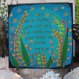 Może przedstawiać: Kwadratowe dzieło sztuki z niebieskim tłem i cytatem "Nie wiem nic na pewno, ale widząc gwiazdy, marzę. - van Gogh." Grafika zawiera żółte gwiazdy i ilustracje roślin.