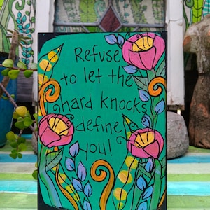 Könnte beinhalten: Handbemaltes rechteckiges Schild mit türkisem Hintergrund und schwarzem Rand. Das Schild zeigt den Text "Refuse to let the hard knocks define you!" umgeben von rosa und gelben Blumen und grünen Blättern.