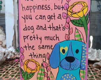 May include: A rectangular wooden sign with a pink background featuring a hand-painted blue dog with a yellow heart on its ear. The text reads: You can't buy happiness, but you can get a dog and that's pretty much the same thing. Yellow flowers surround the dog.