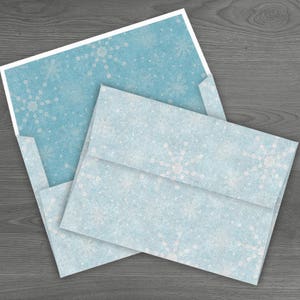 May include: A light blue envelope with a white snowflake pattern. The envelope is folded and has a white border.