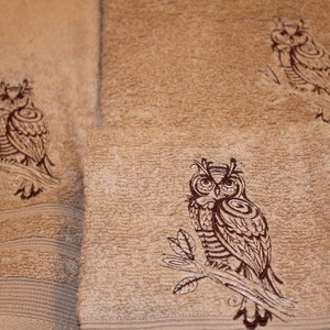 May include: Three brown towels with embroidered brown owls. The owls are perched on branches with detailed feathers and eyes.