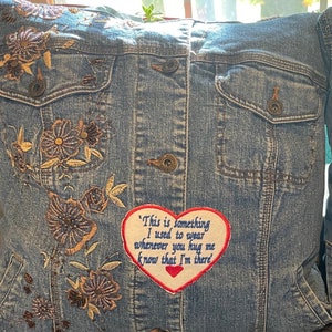 May include: A blue denim pillow with embroidered flowers and a red heart-shaped patch that says "This is something I used to wear whenever you hug me know that I'm there".