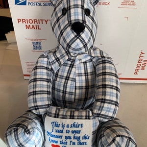May include: A blue and white plaid teddy bear with a pocket on its chest. The pocket has an embroidered message that reads "This is a shirt I used to wear Whenever you hug this know that I'm there. Poppy".