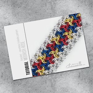 Pode incluir: Uma pulseira artesanal com um padrão triskeles sem costura em vermelho, azul e amarelo, com anéis prateados. A pulseira é exibida em um cartão branco com o texto "Tutorial Moorish Rose". O cartão também inclui o nome do designer.