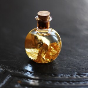 May include: A small glass bottle with a cork stopper filled with a clear liquid and gold flakes.