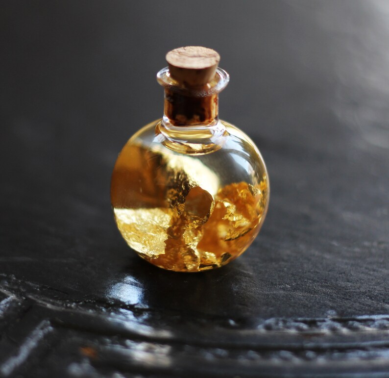 May include: A small glass bottle with a cork stopper filled with a clear liquid and gold flakes.