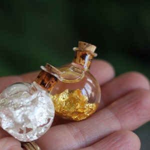 May include: Two small glass bottles with cork stoppers. One bottle is filled with gold flakes and the other with silver flakes.