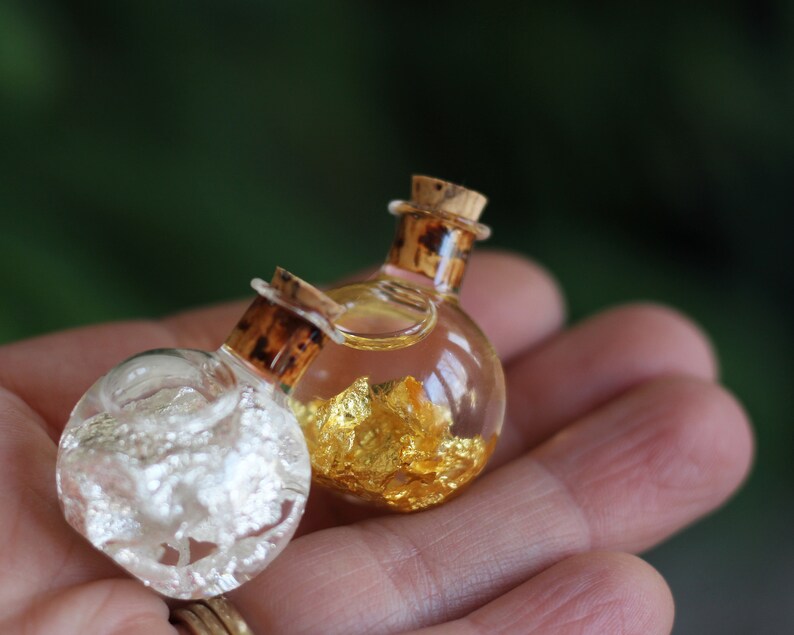 May include: Two small glass bottles with cork stoppers. One bottle is filled with gold flakes and the other with silver flakes.