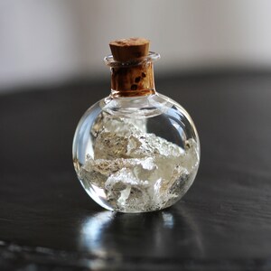 May include: A small, round glass bottle with a cork stopper, filled with silver flakes and a clear liquid.