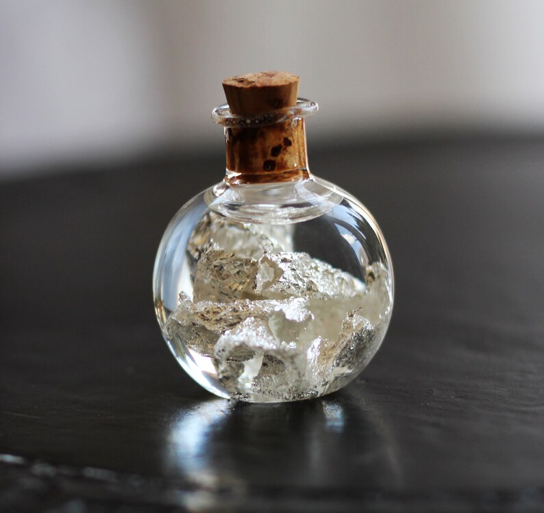 May include: A small, round glass bottle with a cork stopper, filled with silver flakes and a clear liquid.