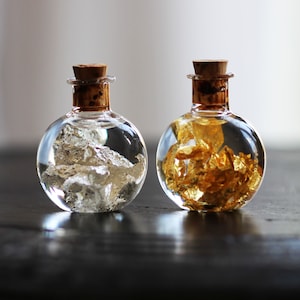 May include: Two round glass bottles with cork stoppers, one filled with silver flakes and the other with gold flakes.