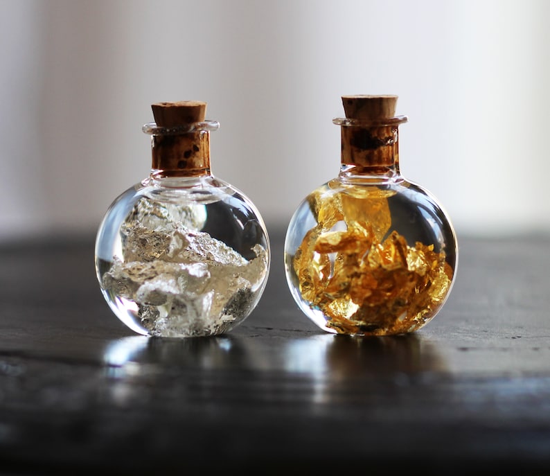 May include: Two round glass bottles with cork stoppers, one filled with silver flakes and the other with gold flakes.