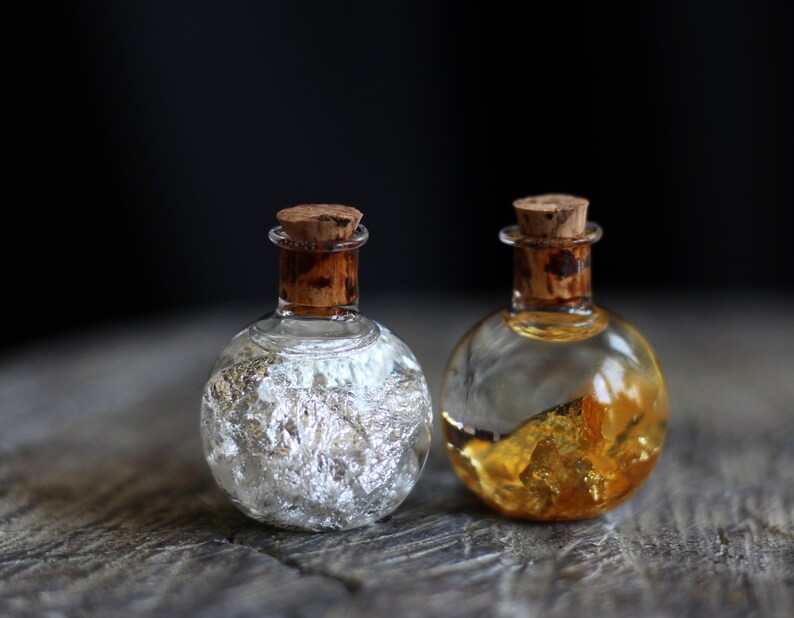May include: Two small glass bottles with cork stoppers. One bottle contains silver flakes and the other contains gold flakes.