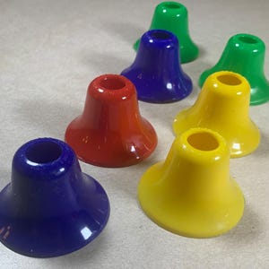 May include: A collection of colorful, cone-shaped objects in various colors: green, blue, red, and yellow. The objects have a flared base and a cylindrical top, arranged on a light-colored surface. The objects appear to be made of a glossy plastic material.