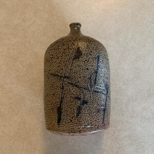 May include: A small, brown ceramic vase with a textured surface and black abstract markings.