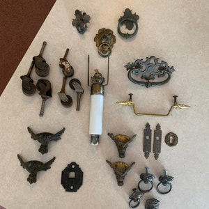 May include: Assortment of antique hardware, including drawer pulls, cabinet knobs, hinges, and furniture casters. The hardware is made of metal and has a variety of finishes, including brass, bronze, and iron.