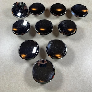 May include: A collection of ten shiny, chrome-finished cabinet knobs. Each knob is round with a slightly domed surface, reflecting light. The knobs are arranged in a grid-like pattern, showcasing their polished appearance and potential for home decor projects.