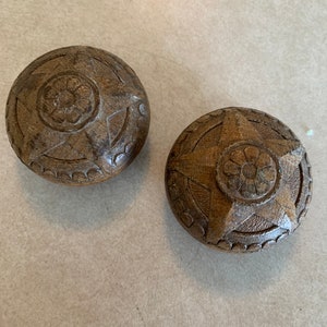 May include: Two wooden knobs with a star and flower design. The knobs are brown and have a rustic look.