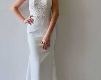 May include: A white sleeveless wedding dress with a high neckline and a lace bodice. The dress has a fitted silhouette and a flowing train.