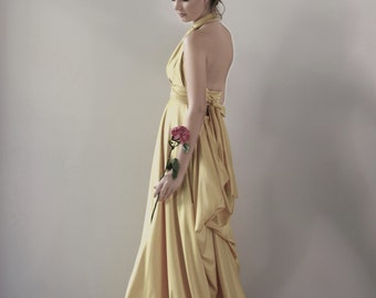 May include: A woman in a yellow satin dress holds a single red rose. The dress has a halter neckline and a flowing skirt.