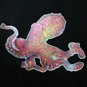 May include: A pink and iridescent octopus with glitter accents. The octopus is depicted in a stylized, cartoon-like manner.