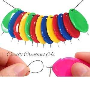 May include: A set of ten colorful plastic threaders with a needle at the end. The threaders are shaped like an oval and have a hole at the top for threading a string. The threaders are strung together on a black string. The image also shows a hand holding a pink threader and threading a black string through the needle.