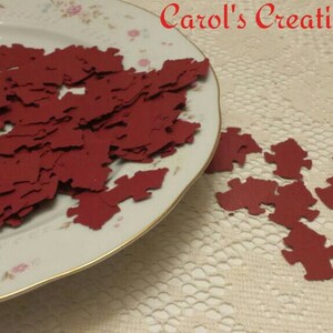 May include: A plate filled with red paper puzzle pieces, with more pieces scattered on a white lace tablecloth. The text "Carol's Creations Az" is visible in the top right corner of the image.