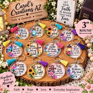 May include: A collection of twelve round, clear acrylic keychains, each 3 inches in diameter, featuring colorful floral designs and inspirational religious text. Each keychain includes a metal ring and a vibrant, solid-colored fabric tassel.