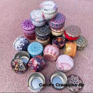 May include: A collection of small, round decorative tins with lids. The tins feature various floral and geometric patterns in colors like purple, blue, pink, and gold. Some lids have the words "Thank you" printed on them.