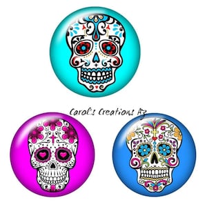 May include: Three round, colorful, glass cabochons with a white sugar skull design. Each skull has a different background color: turquoise, magenta, and blue.