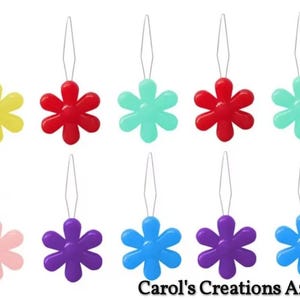 May include: A collection of ten flower-shaped needle threaders in various colors, including yellow, red, teal, pink, purple, and blue. Each threader has a small wire loop for easy threading. The text "Carol's Creations Az" is at the bottom.