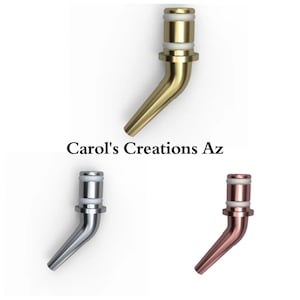May include: Three metal wine bottle pour spouts in gold, silver, and copper colors. Each spout has a curved design with a white band near the top. The text "Carol's Creations Az" is in the center of the image.
