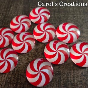 May include: A collection of red and white swirled cabochons, reminiscent of peppermint candies, are scattered across a textured surface. The text "Carol's Creations Az" is visible in the top right corner. These decorative elements are ideal for crafting projects.