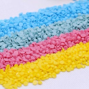 May include: Close-up of colorful round diamond painting beads in yellow, pink, blue, and light blue. The beads are arranged in rows, creating a diagonal pattern.