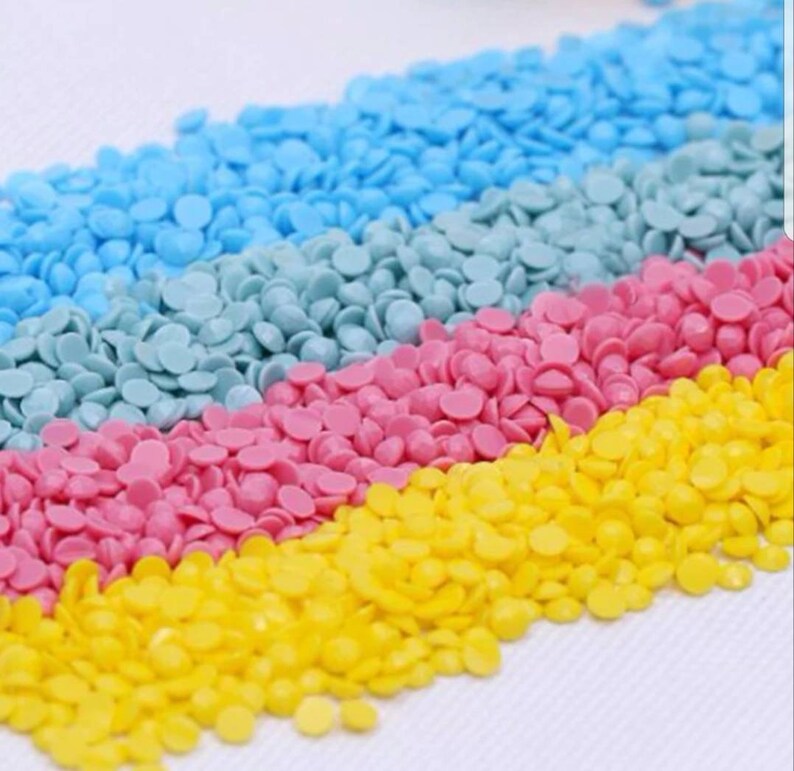 May include: Close-up of colorful round diamond painting beads in yellow, pink, blue, and light blue. The beads are arranged in rows, creating a diagonal pattern.