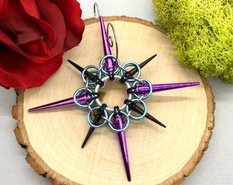 May include: A purple and blue metal star-shaped ornament with black spikes. The ornament is hanging from a silver loop.