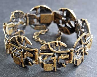 May include: A gold-toned bracelet with a geometric design. The bracelet is made of linked circular pieces with intricate cutouts. The bracelet has a hinged clasp.