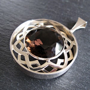 May include: A silver pendant featuring a brown gemstone set within a Celtic knot design.